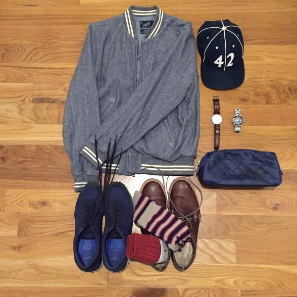 Travel essentials for a cross-country trip. Russel Baseball Jacket by Grayers. Navy sneakers by GREATS Brand. Socks by American Trench. Leather chukka boots by Timberland. Leather watch by Daniel Wellington. Dive watch by Invicta. Vintage ballcap by Goorin Brothers. Dopp kit by Baxter of California.